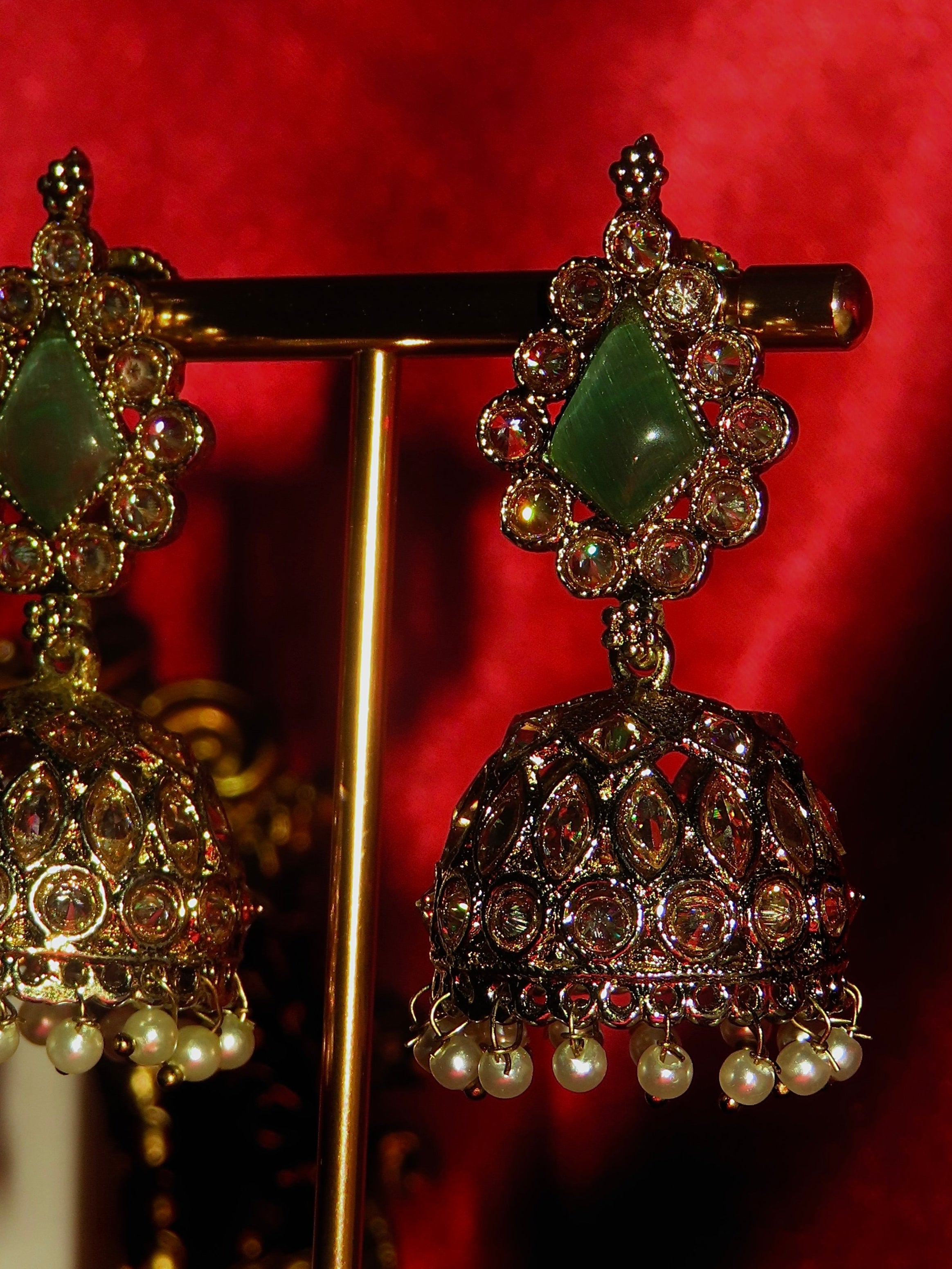 Decorative earrings with green gemstones and pearl-like beads on a red background